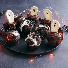 cupcakes decorated with chocolate frosting and ghost heads are on a black plate