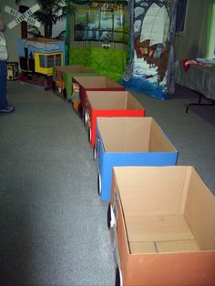 several cardboard train cars are lined up on the floor in an indoor play area with children's toys