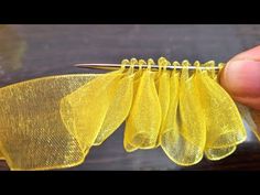 a person holding a pair of scissors in front of some yellow mesh material on a wooden table