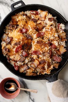 a skillet filled with rice and sausage on top of a marble counter next to a bowl