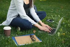 a woman sitting in the grass with her laptop