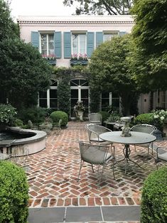 an outdoor patio with tables and chairs in front of a large white building surrounded by greenery