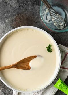 a wooden spoon in a white bowl filled with cream and parsley next to a whisk