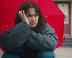 a woman sitting on the ground with an umbrella in front of her, holding her hand to her head