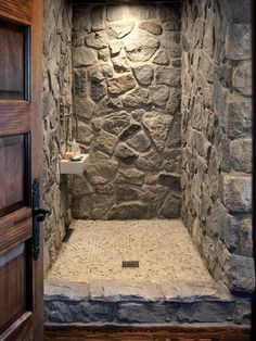 a bathroom with stone walls and flooring is shown in this image, the shower stall has an open door