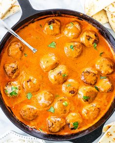 a pan filled with meatballs and sauce next to pita bread on the side