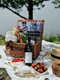 a picnic basket with strawberries, cheese and wine on a blanket by the water