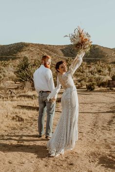 a man and woman are walking in the desert holding bouquets with their hands up