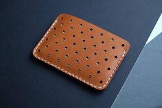 a wallet with holes on it sitting on top of a black table next to a cell phone