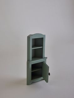 a small green cabinet sitting on top of a white table next to a black object