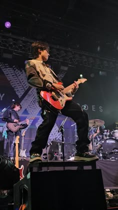 a man standing on top of a stage with an electric guitar in front of him