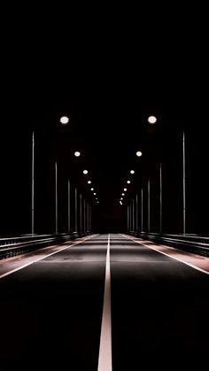 an empty road in the middle of a dark tunnel with lights on either side and one light at the end