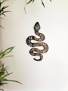 a metal snake is hanging on the wall next to some plants and a potted plant