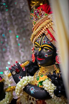 a statue of a person dressed in black and gold with flowers around his neck, holding a pot