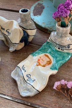 three ceramic vases with flowers in them sitting on a wooden table next to other items