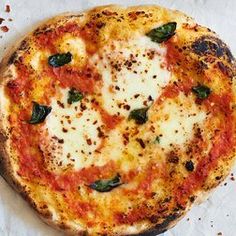 a pizza sitting on top of a white paper covered in cheese and spinach leaves