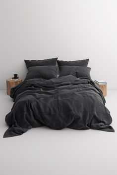 a bed with black sheets and pillows in a white room, next to a night stand