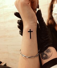 a woman with a tattoo on her arm holding up a wrist cross tattooed in black ink