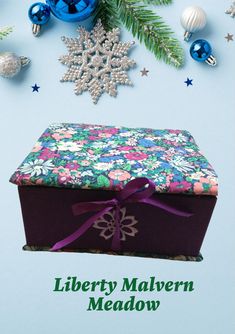 an open box sitting on top of a table next to christmas ornaments and decorations with the words liberty malvenn meadow written below it