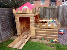 a child's play house made out of pallets and wooden planks in the back yard