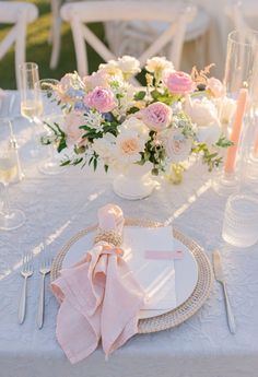 a table set with white and pink flowers, silverware and napkins on it