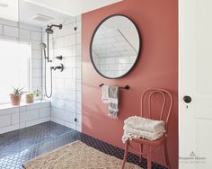 a bathroom with pink walls and white tile flooring, a round mirror on the wall