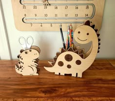 two wooden dinosaurs are on a desk next to a wall clock and pencils holder