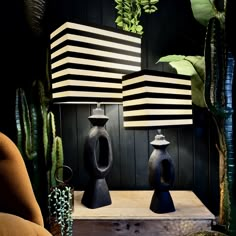 two black vases sitting on top of a wooden table next to a green plant