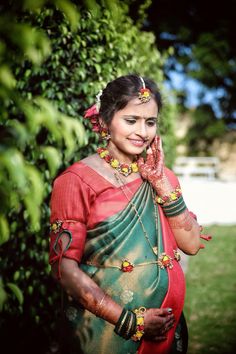 a woman in a red and green sari talking on her cell phone while standing next to a bush