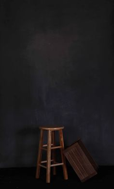 two stools against a black wall and one has a wooden seat on the floor