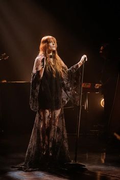 a woman with long red hair is on stage holding a microphone and wearing a black dress