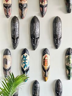 several african masks are hanging on the wall next to a potted plant and some plants