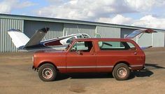 an old red pick up truck parked in front of a hangar with a small plane