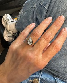 a woman's hand with a diamond ring on top of her left hand, sitting next to a pair of jeans