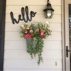 flowers in a basket hanging on the side of a house next to a lamp and door