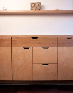 a wooden cabinet with four drawers and two clocks on the top shelf, in front of a white wall