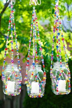 three mason jars hanging from a tree filled with colorful beaded beads and candle holders