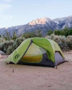 a tent pitched up on the ground with mountains in the background