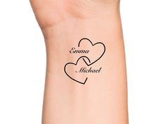 two hearts tattoo on the wrist that says, comma and micheal in black ink