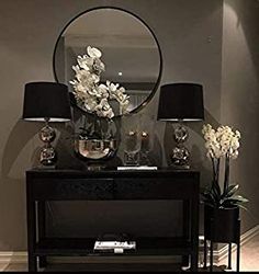 a black table topped with two lamps next to a mirror and vase filled with flowers