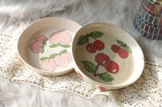 two bowls with cherries painted on them are sitting on a white furnishing