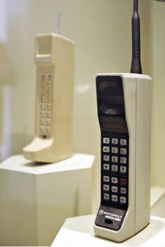 an old cell phone sitting on top of a white pedestal next to a telephone receiver