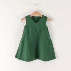 a green dress hanging on a hanger against a white wall with a wooden hanger