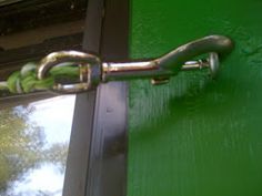 a green door with a metal chain hanging from it's side and a window in the background