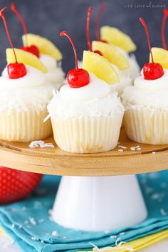 pineapple cupcakes with white frosting and cherries on a cake plate