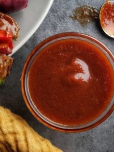 a bowl of sauce next to a sandwich on a plate with pickles and ketchup