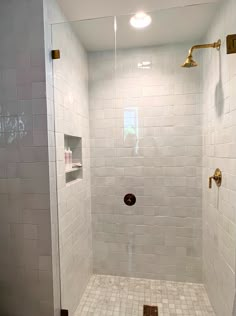 a walk in shower sitting next to a white tiled wall and floor with gold fixtures