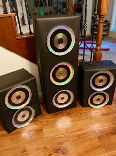 three speakers are sitting on the floor in front of a stair case, and one is black with multi - colored trim