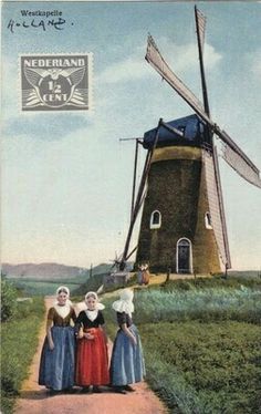 three women standing next to each other in front of a windmill on a country road