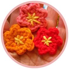 three crocheted flowers are in the palm of someone's hand with a pink circle around them